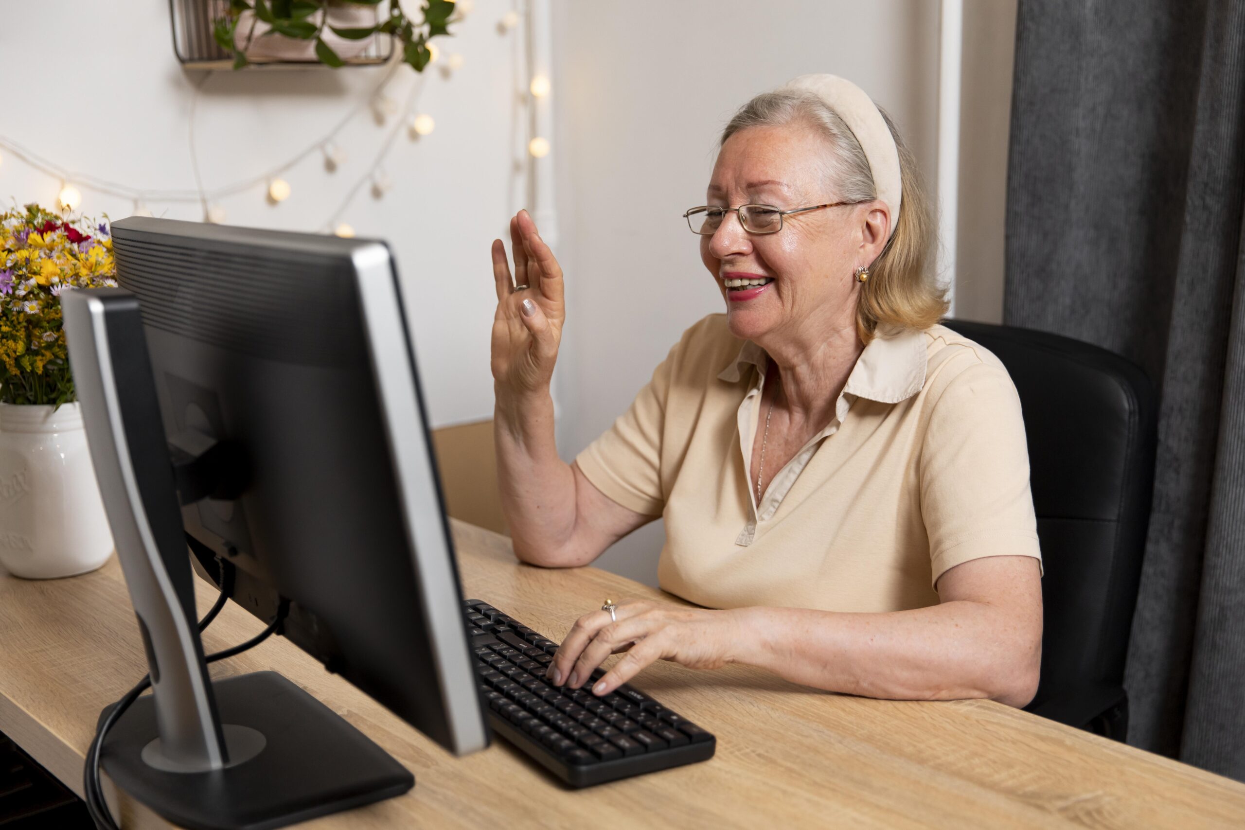 A senior woman smiling and waving at a computer screen