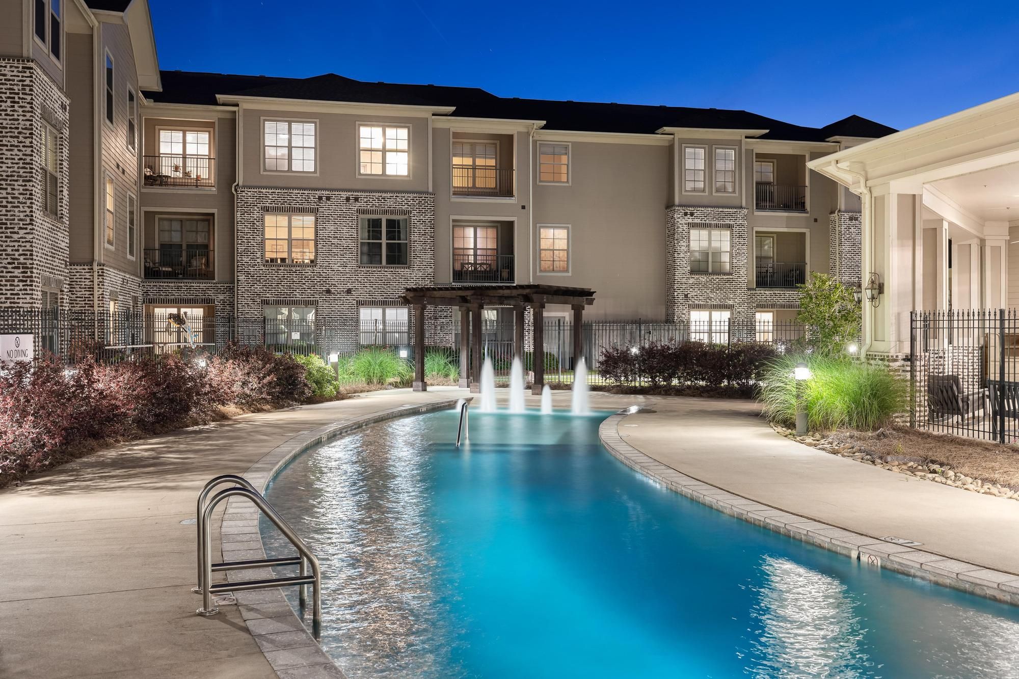 The Claiborne at Hattiesburg senior apartment pool lit at night with fountain and terrace
