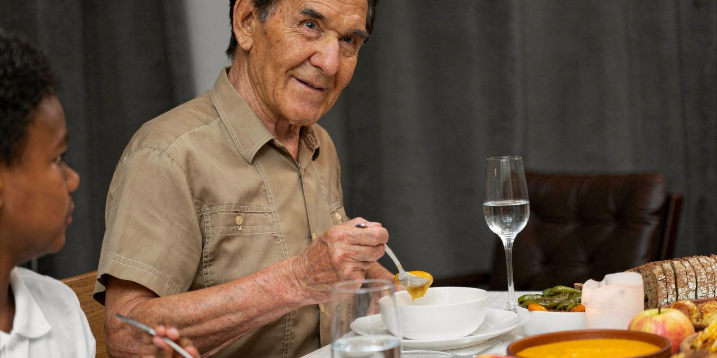 An elderly man eats soup at a dinner table, sitting beside a child, with food and drinks in front of them.