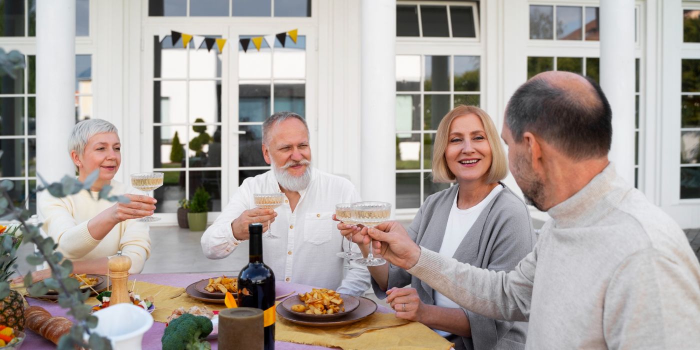Four older adults sit outdoors at a table, smiling and raising glasses in a cheerful toast.