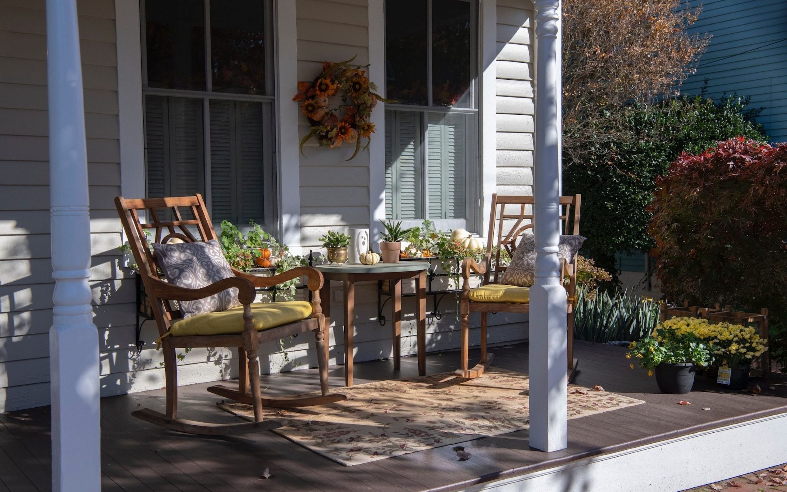 Front porch with two wooden rocking chairs, a small table, plants, and fall wreath on the window.