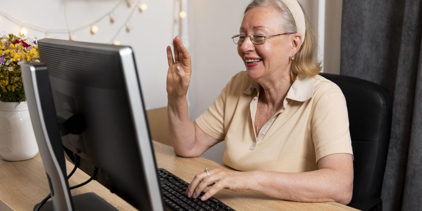 A senior woman smiling and waving at a computer screen