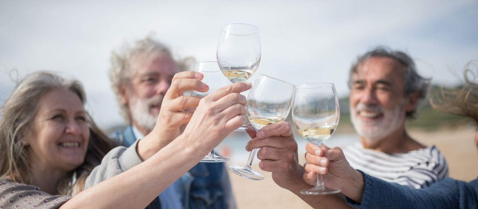 Happy senior friends toasting with white wine on the beach