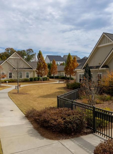 Sidewalk winding through a suburban neighborhood with houses, lawns, shrubs, and autumn trees.