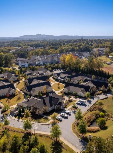 Aerial view of a suburban neighborhood with houses, trees, and distant hills under a clear blue sky.