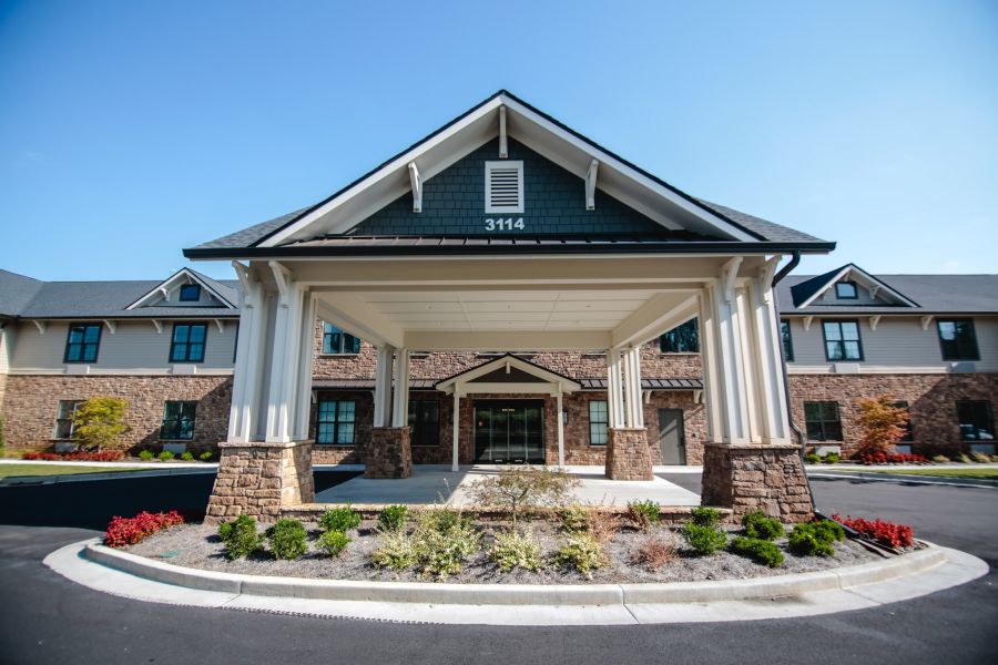 Front view of Brickmont at Woodstock's entrance with a covered driveway, stone accents, and landscaped greenery.