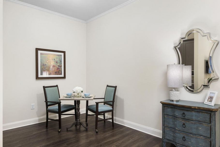 Small dining area with a table set for two, floral centerpiece, artwork on the wall, and a decorative mirror nearby.