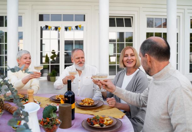 Four older adults sit outdoors at a table, smiling and raising glasses in a cheerful toast.