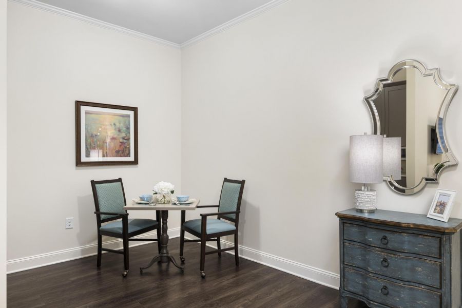 Small dining area with a table set for two, floral centerpiece, artwork on the wall, and a decorative mirror nearby.