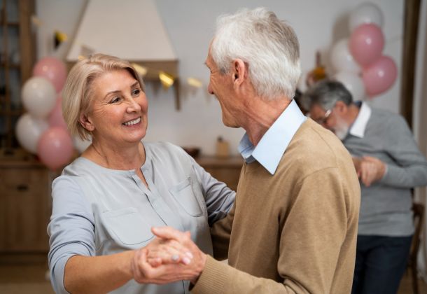 Smiling older couple dancing together at a party with balloons and another couple in the background.