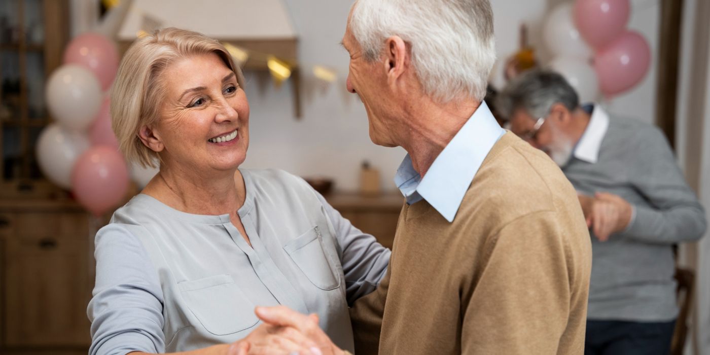 Smiling older couple dancing together at a party with balloons and another couple in the background.