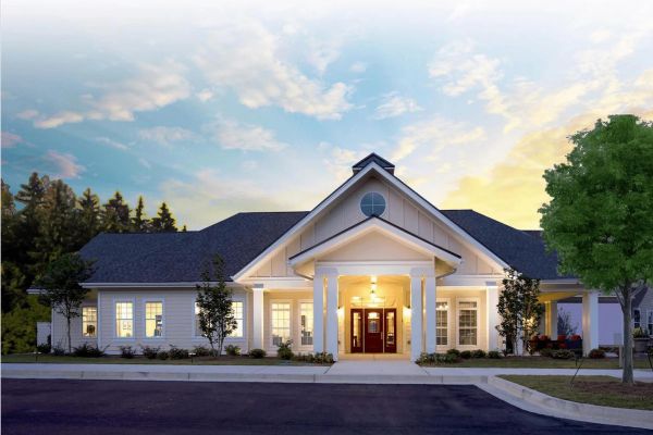 Single-story white building with columns, lit entrance, and a tree, under a sunset sky.