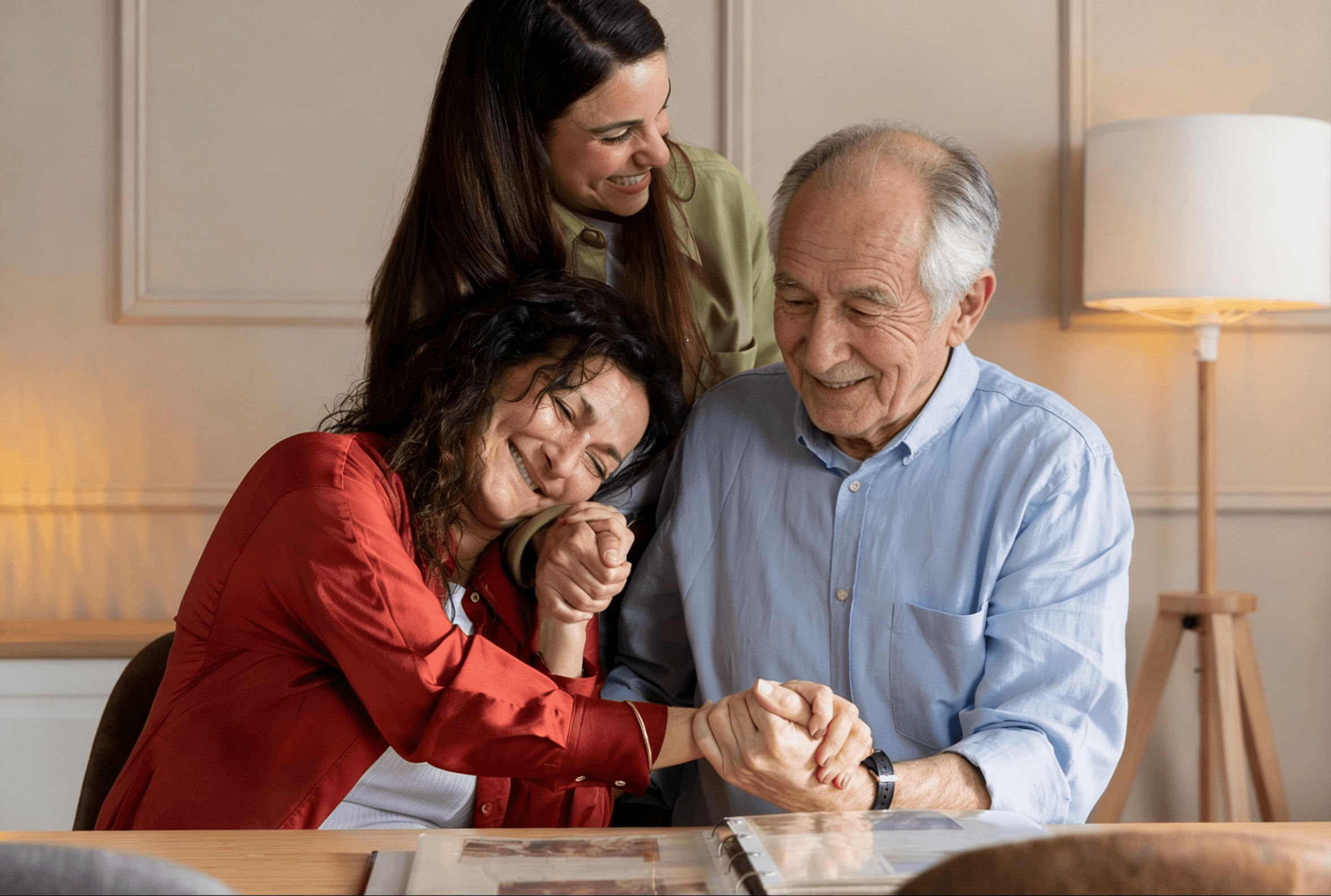 Three people smiling and holding hands while looking at a photo album at a table.