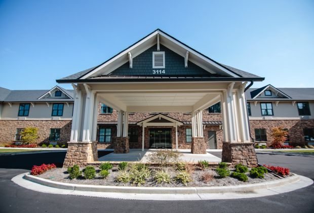 Front view of Brickmont at Woodstock's entrance with a covered driveway, stone accents, and landscaped greenery.