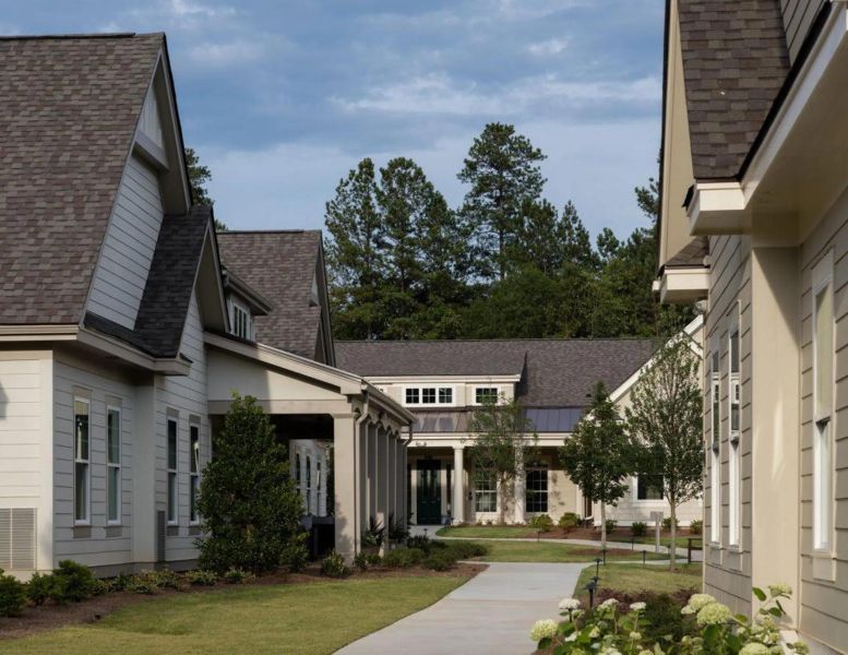 A sidewalk runs between modern houses with peaked roofs, surrounded by trees and landscaping.