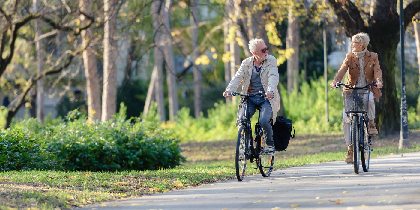Active senior couple riding bicycles through a paved park path