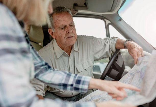 An older man and woman sit in a vehicle, looking closely at a paper map and discussing directions.