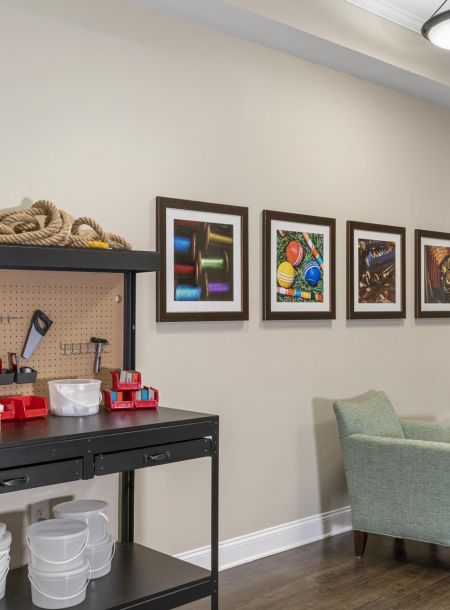 Workshop space with tools on shelves, wall art, two green chairs, and a wall-mounted cabinet.