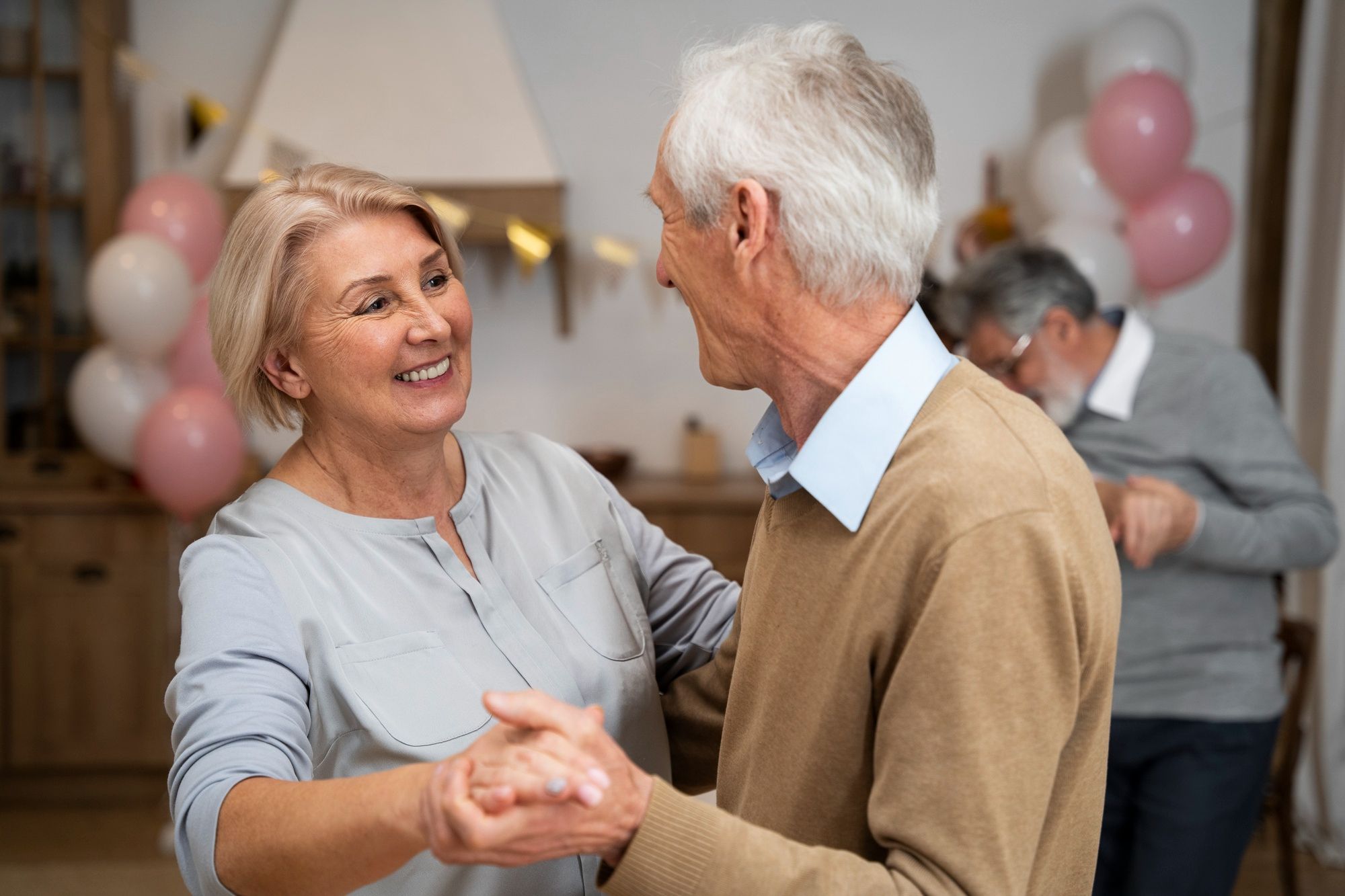 Smiling older couple dancing together at a party with balloons and another couple in the background.