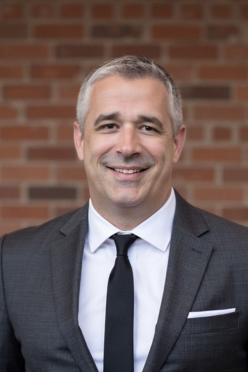 Smiling man in a suit and tie standing in front of a brick wall.