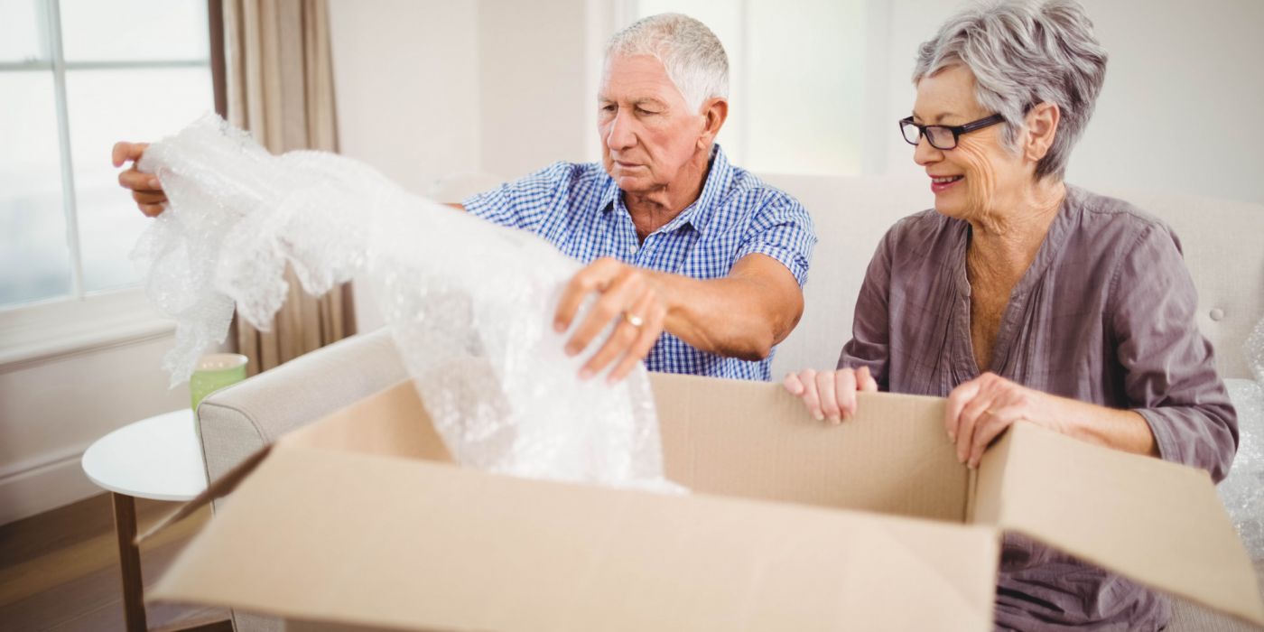 Smiling older couple unpacking a cardboard box and bubble wrap in their living room.