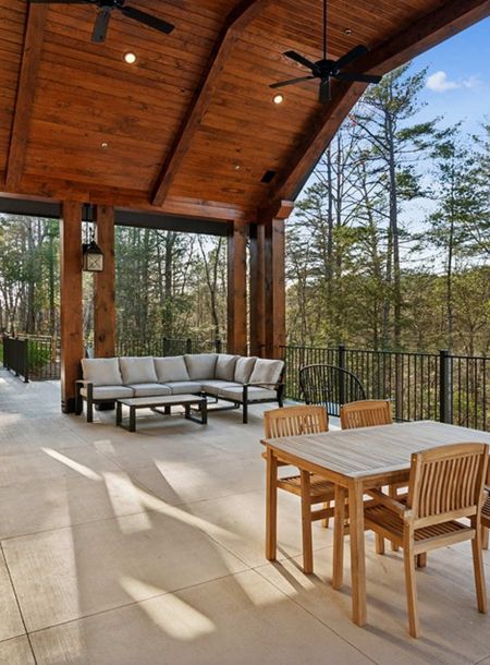 Covered patio with a dining table and outdoor sectional sofa overlooking a forest.