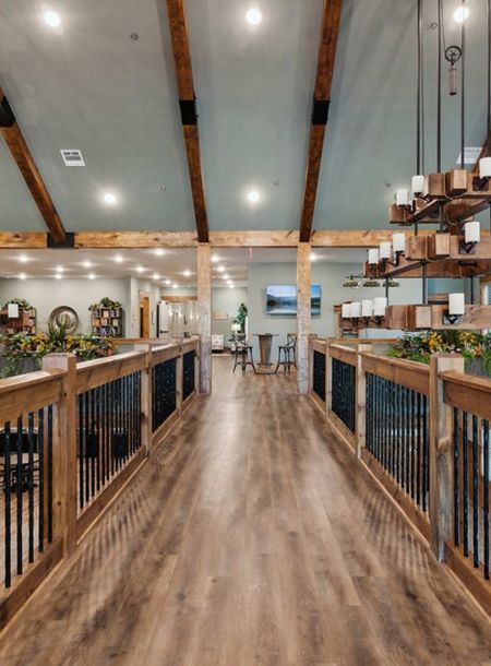 A raised wooden walkway with metal railings overlooking a room with large tiered chandeliers and exposed ceiling beams.