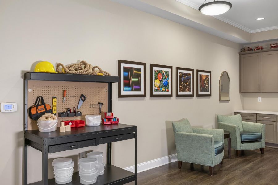 Workshop space with tools on shelves, wall art, two green chairs, and a wall-mounted cabinet.