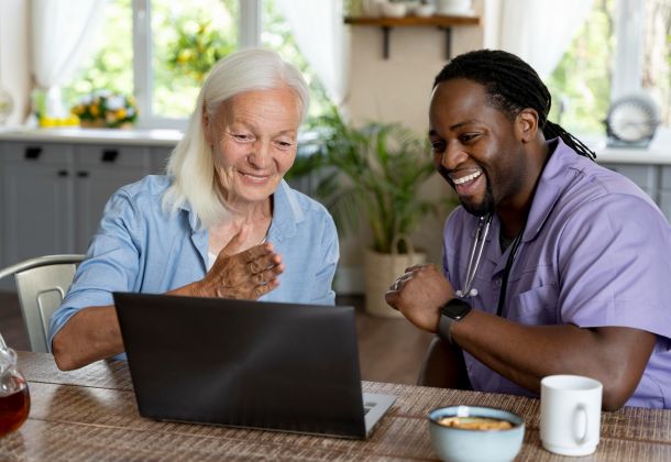 A senior woman and health worker smiling and looking at a computer together.