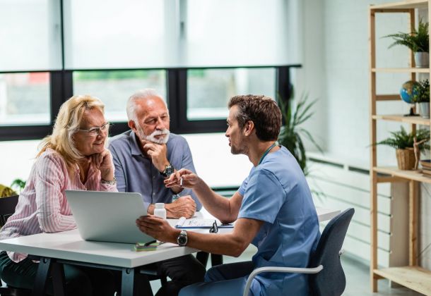 A doctor discusses something with an older couple at a desk in a bright, modern office.