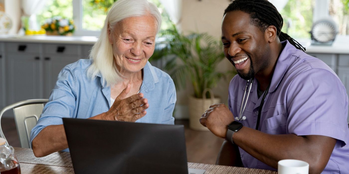 A senior woman and health worker smiling and looking at a computer together.