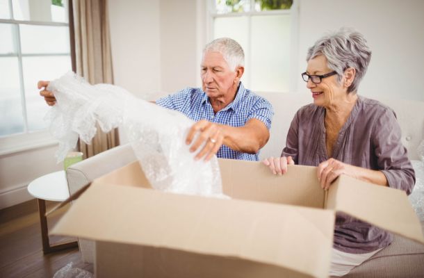 Smiling older couple unpacking a cardboard box and bubble wrap in their living room.