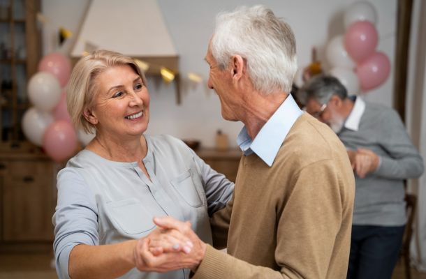 Smiling older couple dancing together at a party with balloons and another couple in the background.