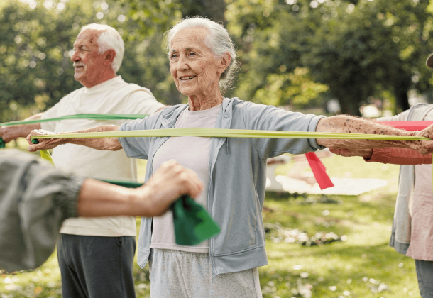 Seniors exercising outdoors with resistance bands, smiling and standing in a park.