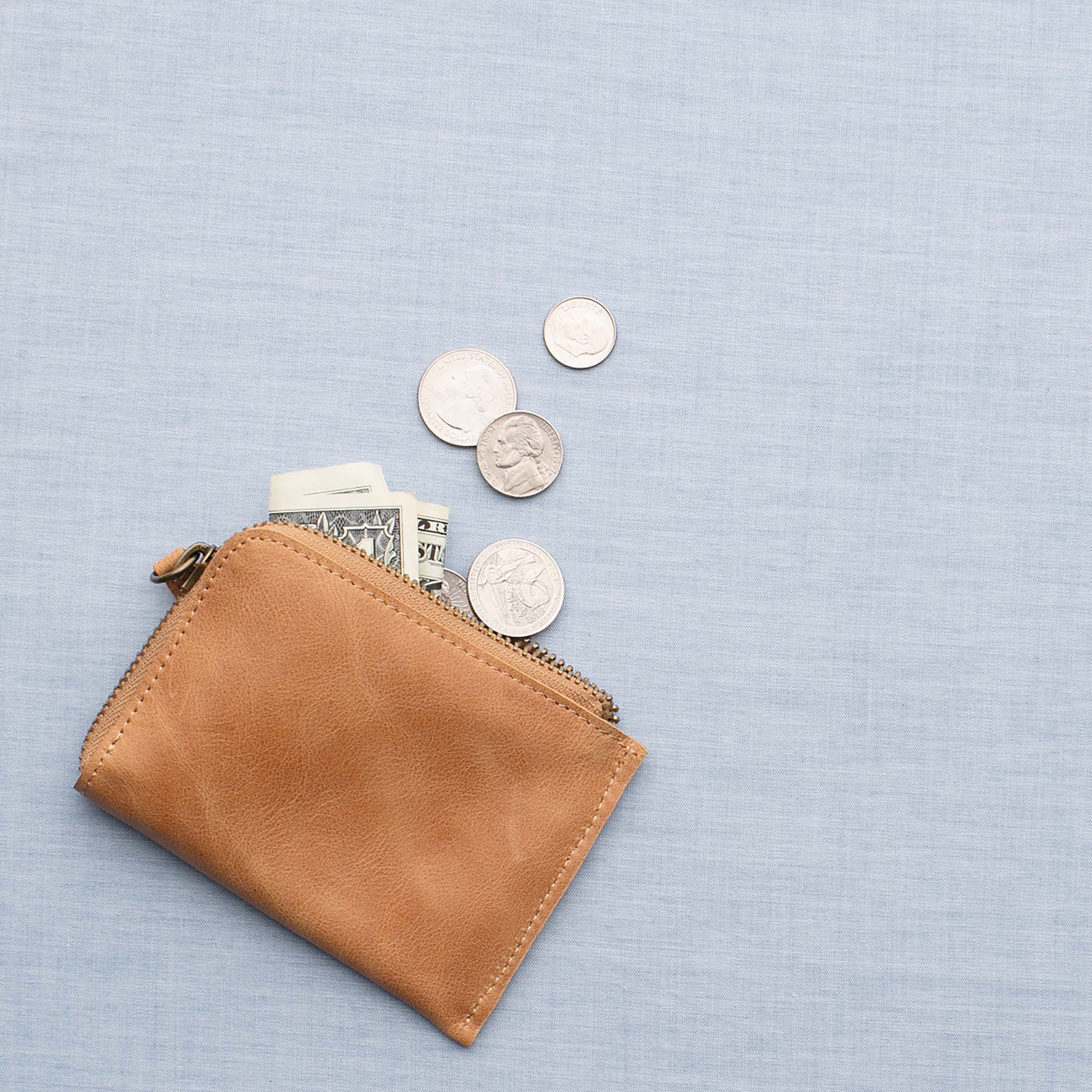 Tan leather wallet with dollar bills and coins spilling out.