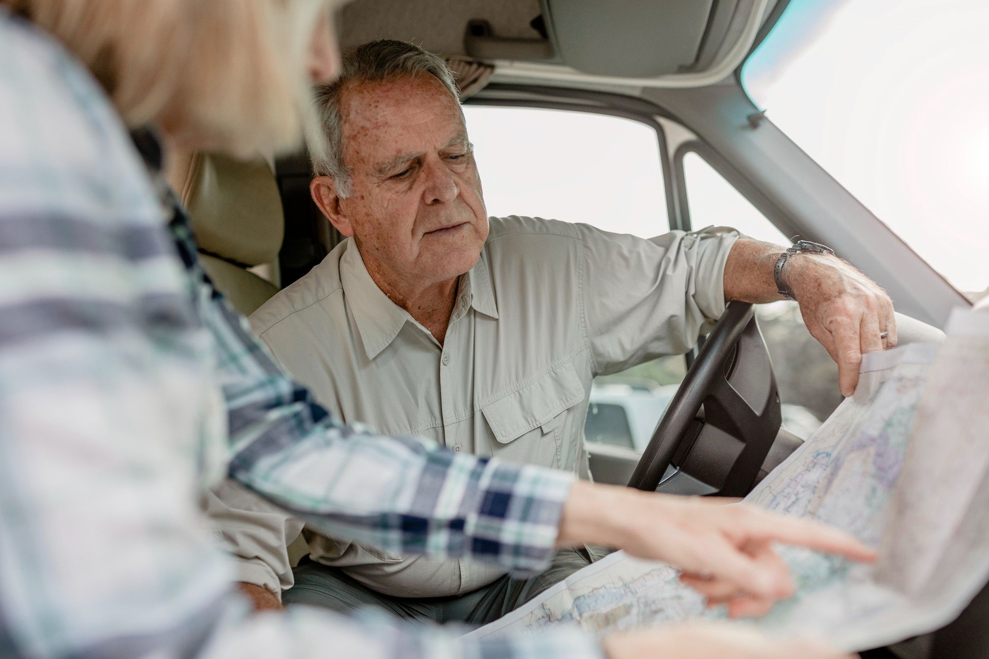 An older man and woman sit in a vehicle, looking closely at a paper map and discussing directions.