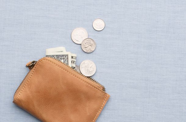 Tan leather wallet with dollar bills and coins spilling out.