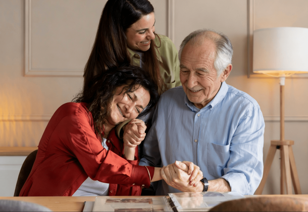 Three people smiling and holding hands, gathered around a table with a photo album.