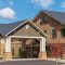 Brickmont at Johns Creek with stone facade, dark roof, covered entrance, and a small tree in front. Blue sky with clouds.