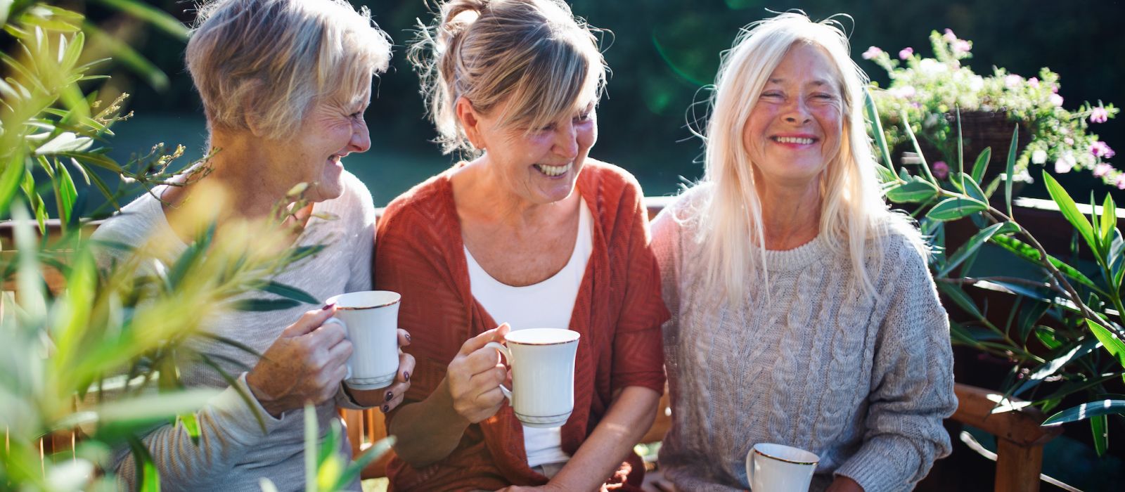 Group of senior women friends with coffee sitting outdoors on terrace, resting.