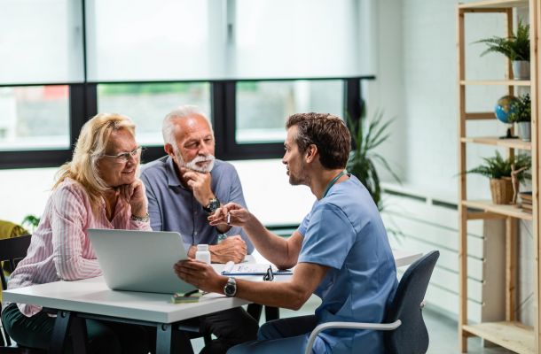 A doctor discusses something with an older couple at a desk in a bright, modern office.