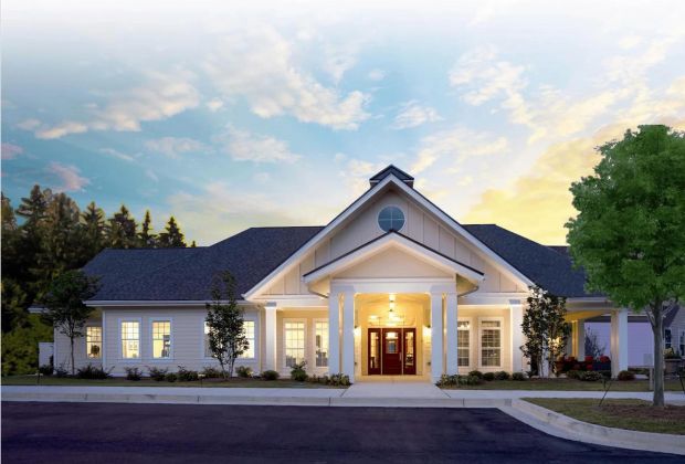 Single-story white building with columns, lit entrance, and a tree, under a sunset sky.