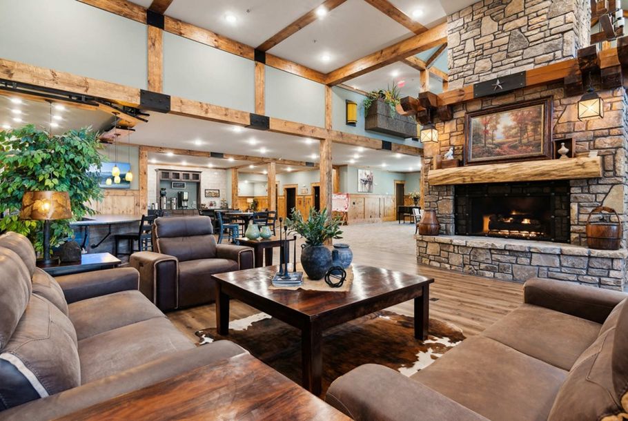 Rustic lodge lobby featuring a stone fireplace, wood-beam ceiling, and comfortable brown seating areas.