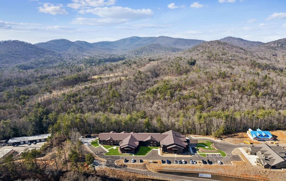 Aerial view of a complex of buildings nestled in a forest at the base of mountain ranges.