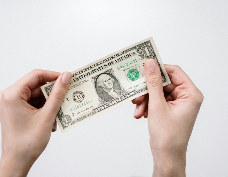 Two hands holding a US one-dollar bill against a plain white background.