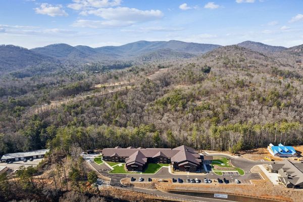 Aerial view of a complex of buildings nestled in a forest at the base of mountain ranges.