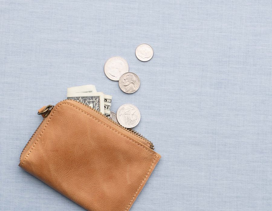 Tan leather wallet with dollar bills and coins spilling out.