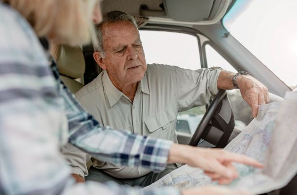 An older man and woman sit in a vehicle, looking closely at a paper map and discussing directions.
