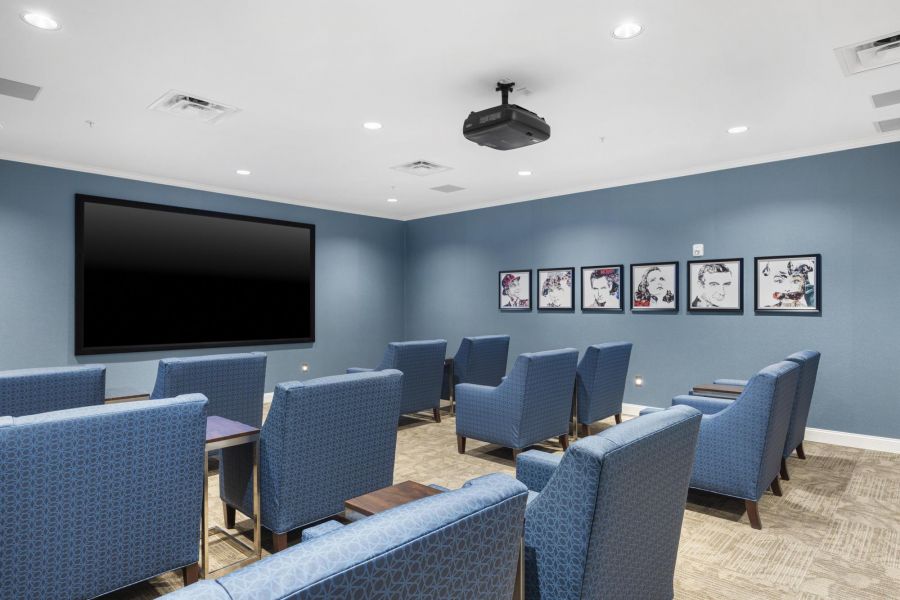 A small theater room with blue armchairs, a large screen, and framed artwork on blue walls.