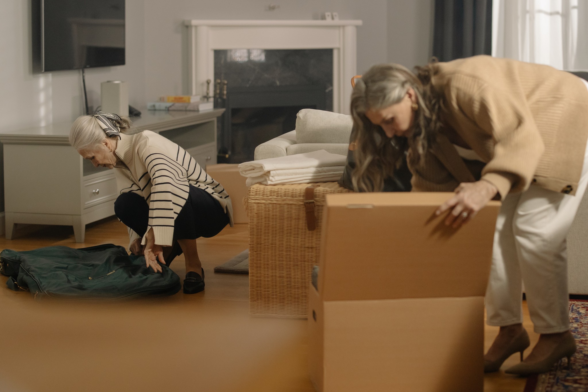 Two women packing boxes in a living room